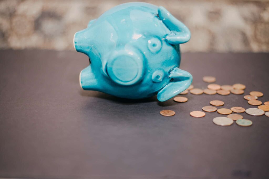 Imagem de um porco mealheiro deitado de lado e moedas espalhadas - poupar