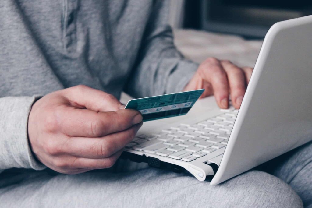 mãos de um homem, uma no portátil e outra segura um cartão de crédito