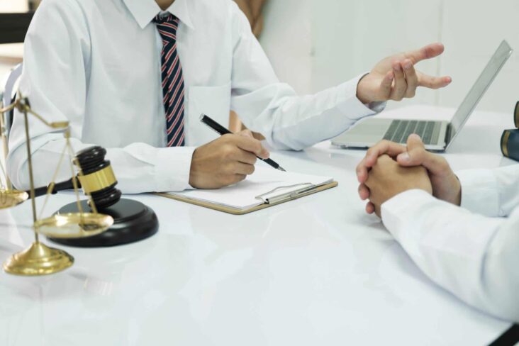 dois jovens, executivos, roeados por sínbolos da Justiça, como o martelo e a balança, assinam documentos sobre os processos de doação e herança a ilustrar: Heranças: Saiba como receber?