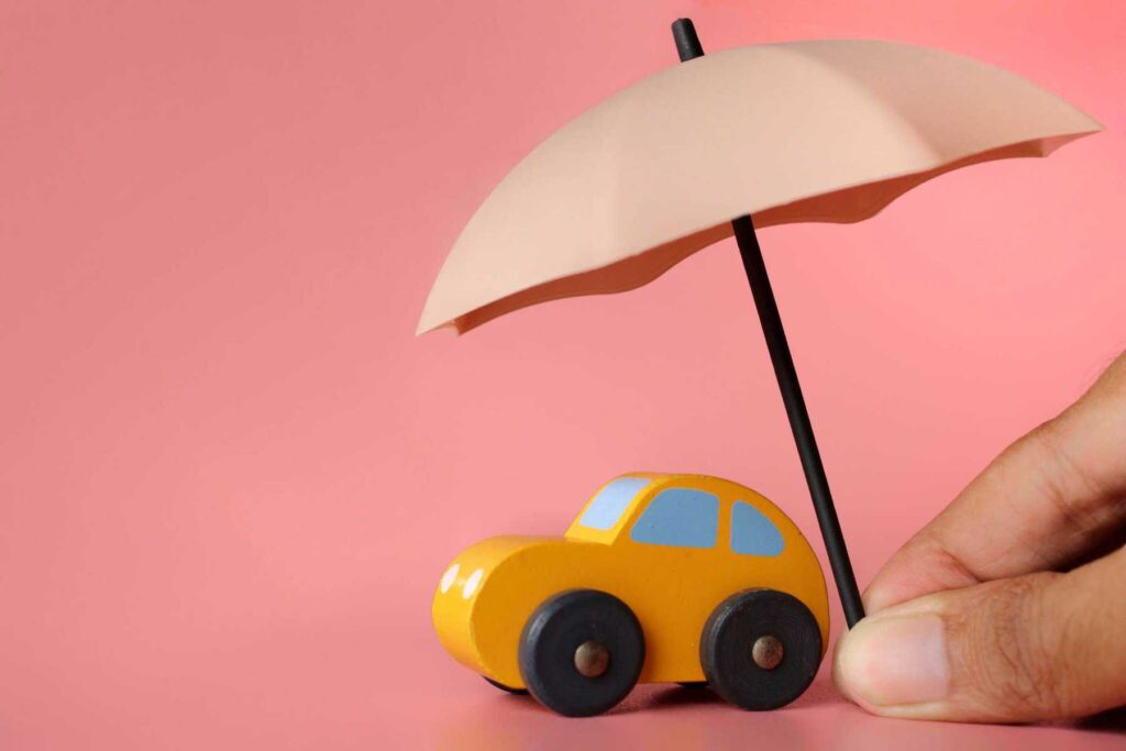 carro amarelo em miniatura. Por cima está um chapéu de chuva, numa alusão ao seguro auto