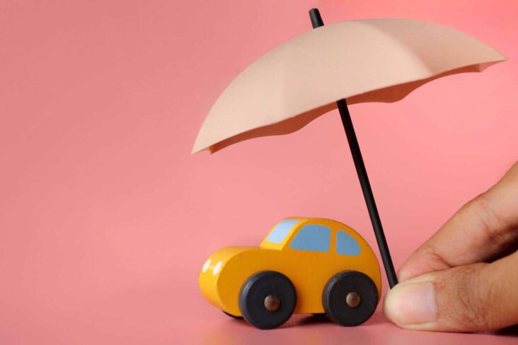 carro amarelo em miniatura. Por cima está um chapéu de chuva, numa alusão ao seguro auto