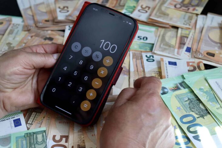 pessoa com uma calculadora na mão com notas de euros de fundo a ilustrar como poupar em 2025