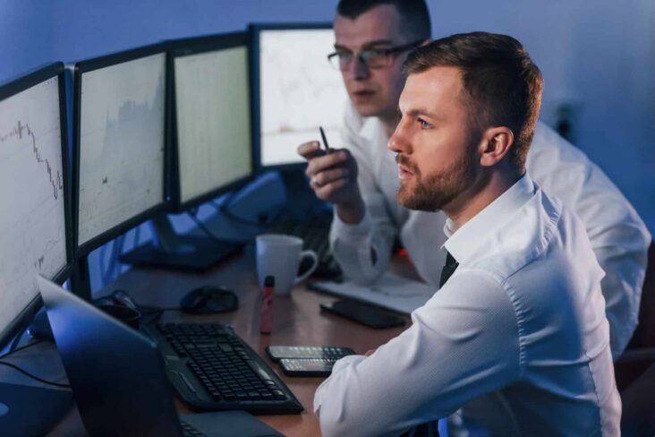 Dois traders de bolsa analisam dados para tomarem decisões de investimentos