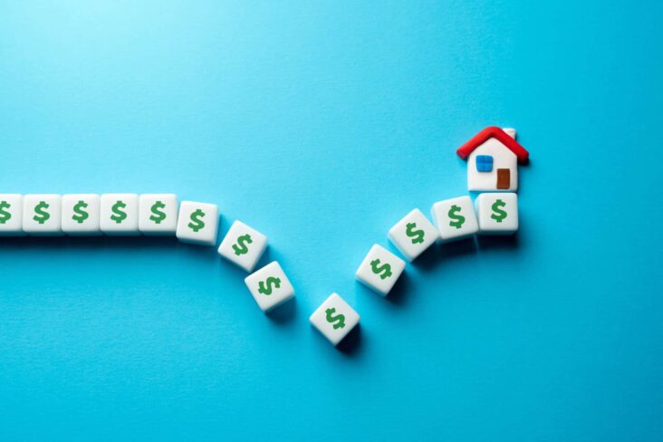 Vários dados, com símbolo de juros gravados, alinhados, fazendo um gráfico de variação das taxas de juro. No final surge uma casa em miniatura, numa alusão ao que esperar do imobiliário em 2025