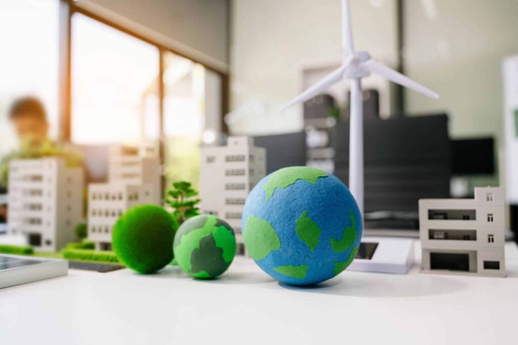 10 dicas ajudar a cuidar do nosso bem comum: A Terra Três bolas com o planeta terra desenhadas dentro de uma estrutura miniatura onde se veem prédios e soluções de energias renováveis, como o solar ou a eólica