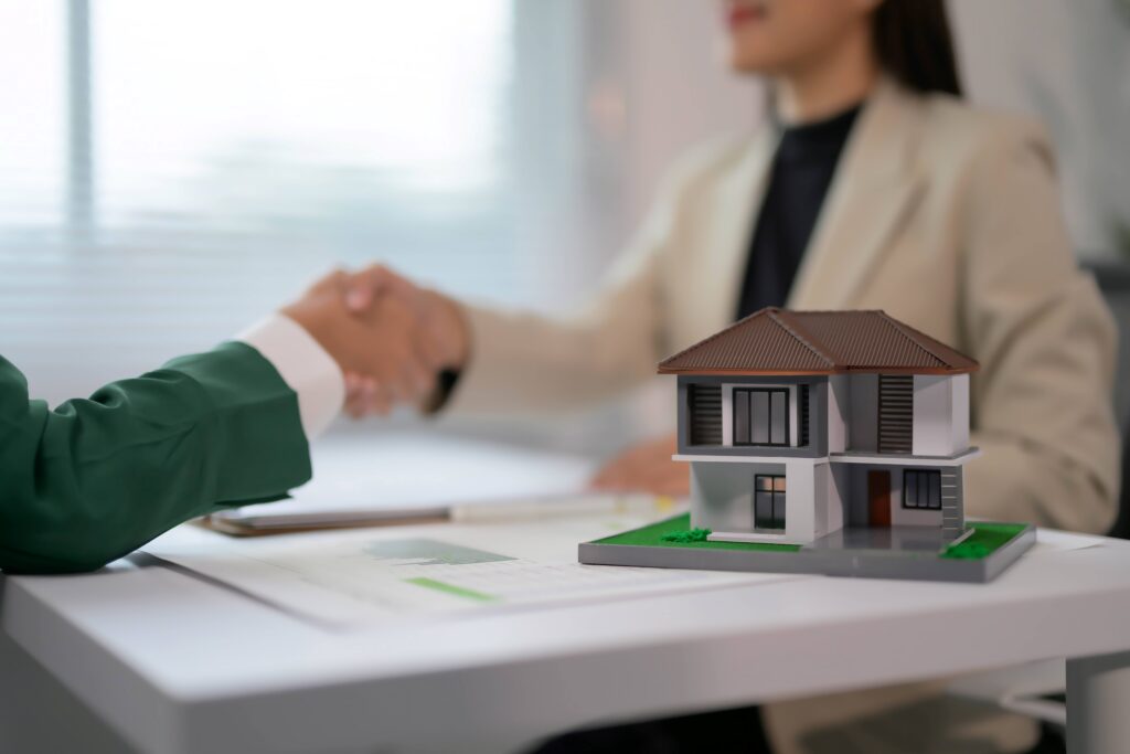 Crédito habitação regressa às vésperas da crise financeira e toca em máximos de 16 anos Agente imobiliário apertando a mão do cliente sobre modelo de casa na mesa em um ambiente de escritório moderno