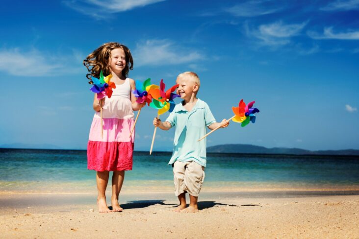 Dois irmãos na praia, com moinhos de papel.