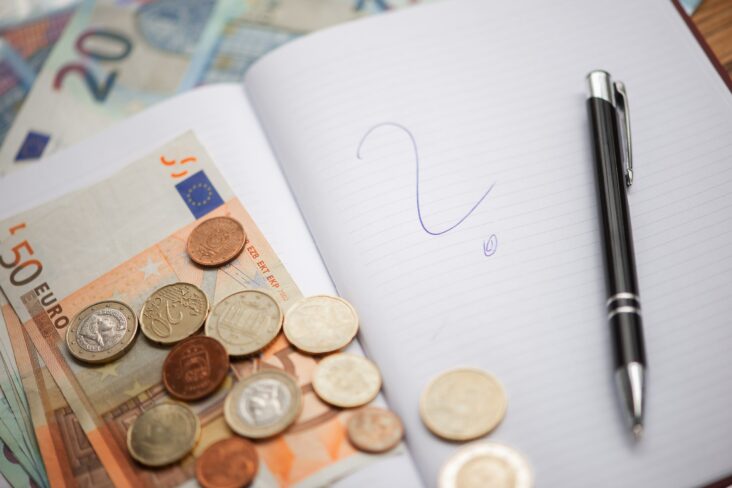 Notas de 50 euros e algumas moedas espalhadas em cima de um caderno onde se pode ver um ponto de interrogação desenhado a caneta, numa alusão às dúvidas sobre o impacto nos rendimentos.