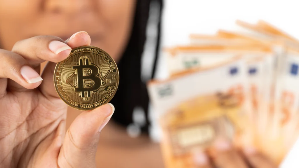 Mulher agarra uma moeda com o logótipo da Bitcoin, e várias notas de cinquenta euros