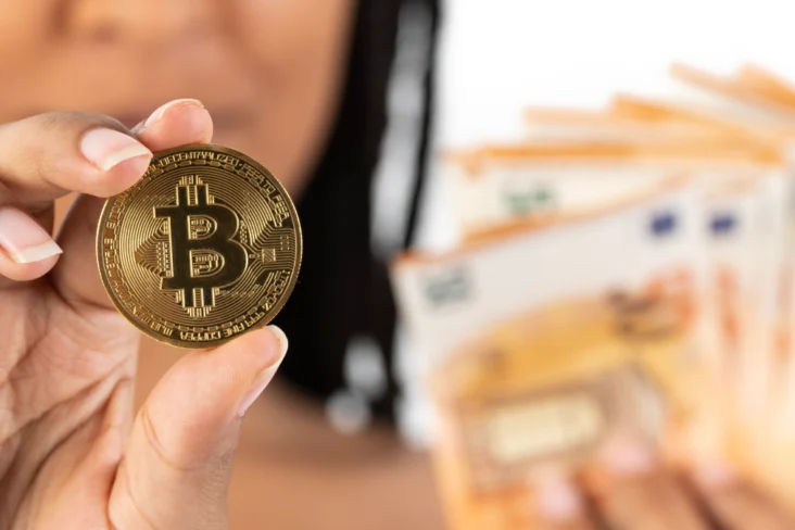 Mulher agarra uma moeda com o logótipo da Bitcoin, e várias notas de cinquenta euros