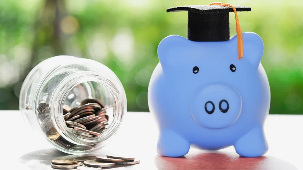 Crédito para pagar propinas: Como funciona? Porquinho mealheiro azul com chapéu de graduação ao lado de um frasco de vidro cheio de moedas