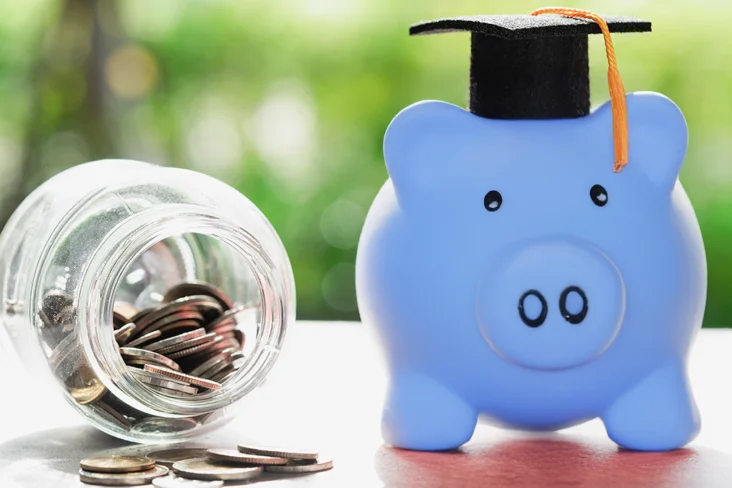 Porquinho mealheiro azul com chapéu de graduação ao lado de um frasco de vidro cheio de moedas