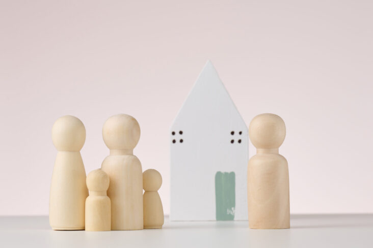 Figuras em madeira que representam pessoas e uma família. Por trás, uma casa, numa alusão a herança