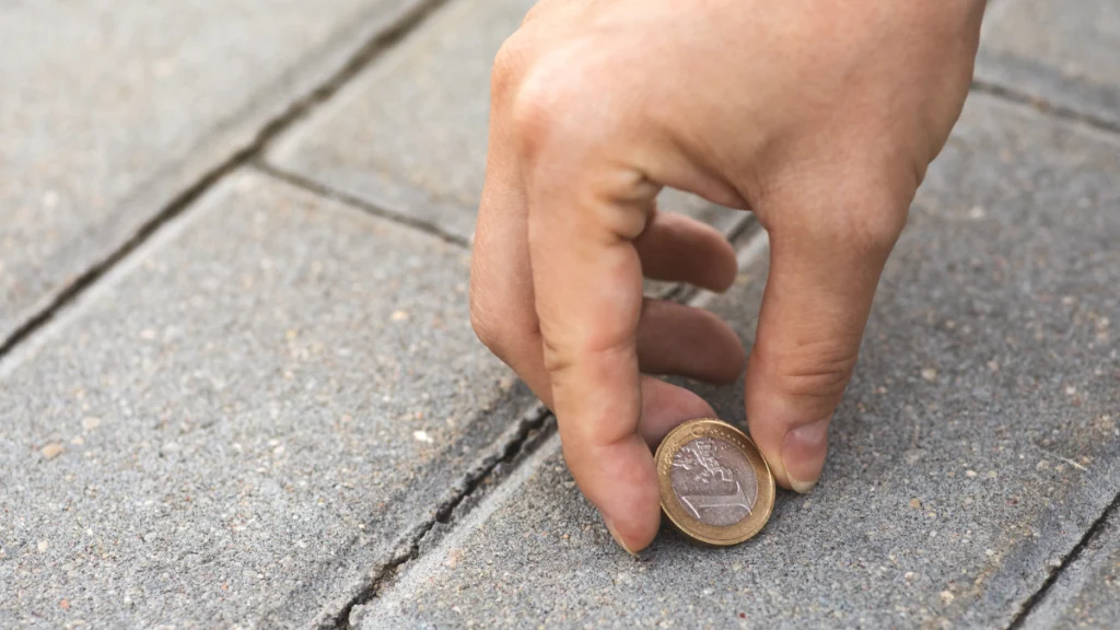 Pessoa a apanhar uma moeda de um euro do chão de tijolo