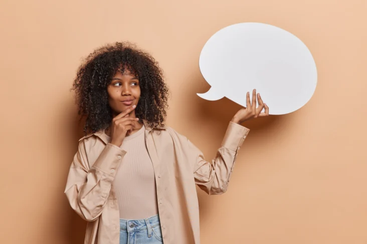 Mulher segura num balão de fala feito de papel, enquanto posa com uma careta pensativa