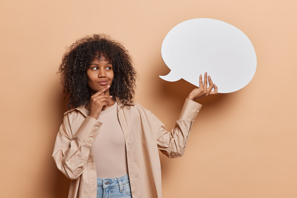 Mulher segura num balão de fala feito de papel, enquanto posa com uma careta pensativa