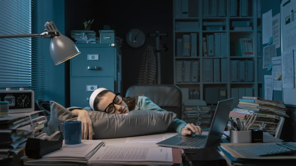 Mulher exausta adormece à secretária no escritório do seu emprego