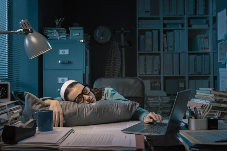 Mulher exausta adormece à secretária no escritório do seu emprego